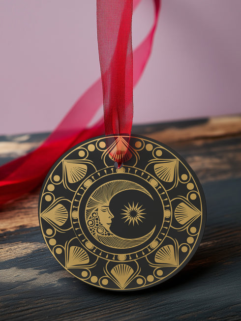 Round metal ornament featuring a golden crescent moon face with star detail, surrounded by art deco shell motifs on black background. 3.5-inch diameter double-sided design with lunar phase pattern and crimson ribbon attachment. Vintage-inspired celestial artwork.